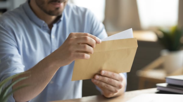 Close up young man opening envelope with paper correspondence. Curious businessman getting paper document by postal service or financial notification at workplace, received notification or invitation